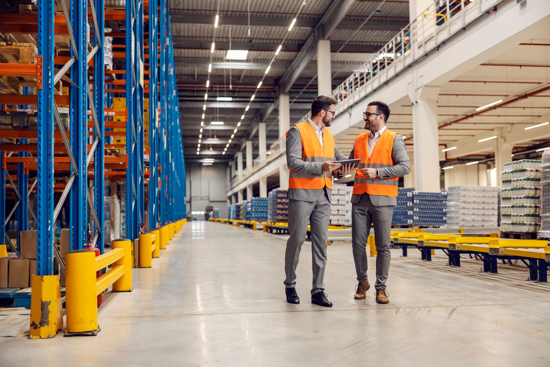 Two factory managers walk in warehouse and check on goods on tablet.
